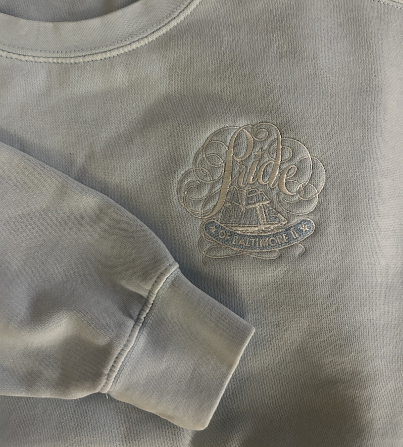 Product Description: A soft, light-blue Comfort-Dyed crewneck featuring Pride of Baltimore’s heritage logo embroidered in crisp white. Cozy, durable, & effortlessly classic — perfect for showing your Pride of Baltimore II spirit year-round.</br> Crewneck Sweatshirt (Light Blue)